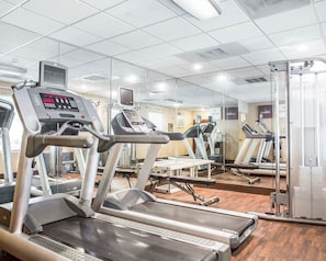 Un gimnasio con cintas de correr, equipo de ejercicio y un espejo grande.