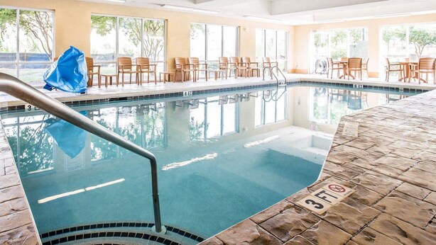Une piscine intérieure à l’eau claire, avec une indication de la profondeur (environ 90 cm) et des chaises longues en bois disposées autour de la piscine.