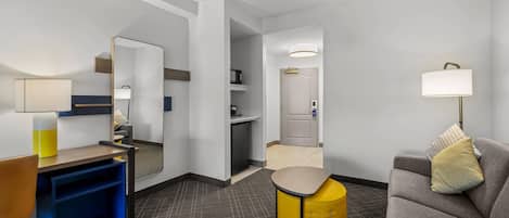 Una habitación de hotel con escritorio, silla, sofá y un taburete amarillo pequeño.