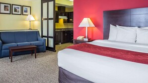 Une chambre d’hôtel avec un lit, un canapé bleu, une petite table, une table de chevet avec une lampe et une vue sur la cuisine.