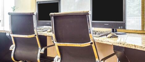 Three office chairs with black and gold accents, a desktop computer, and a keyboard on a desk in a room with large windows.