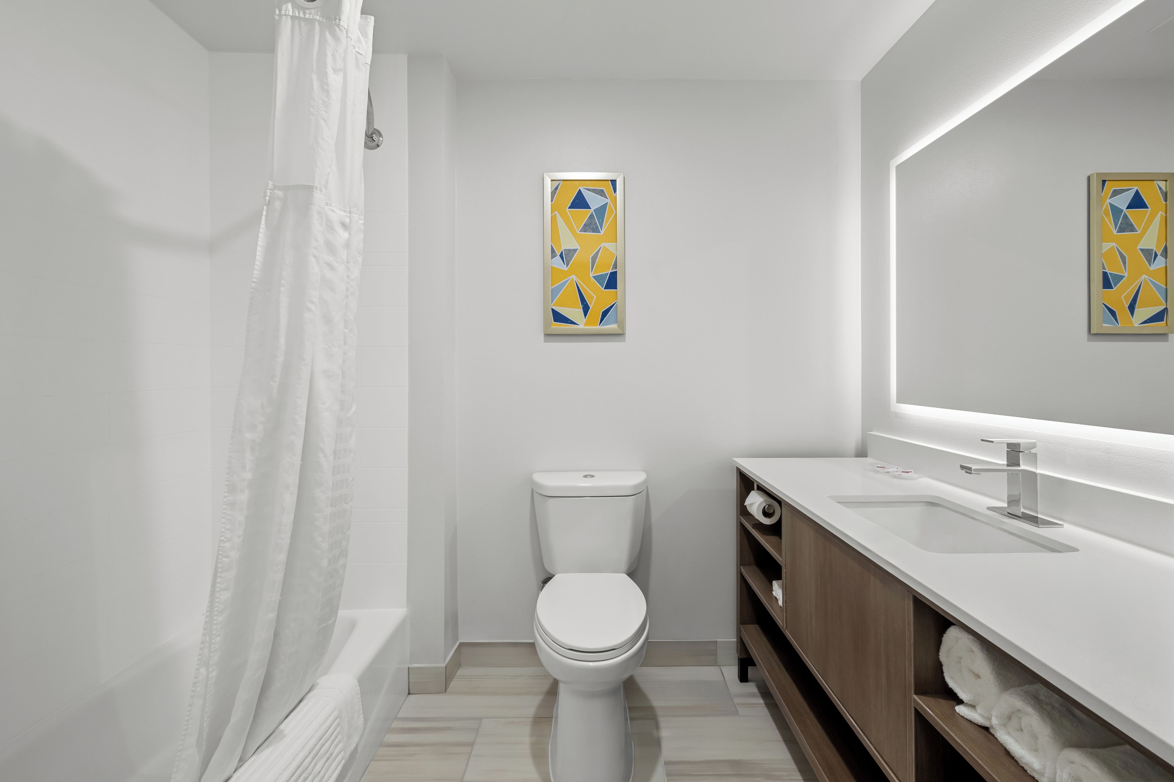 A modern bathroom with a toilet, a shower with a white curtain, and two framed wall art pieces.