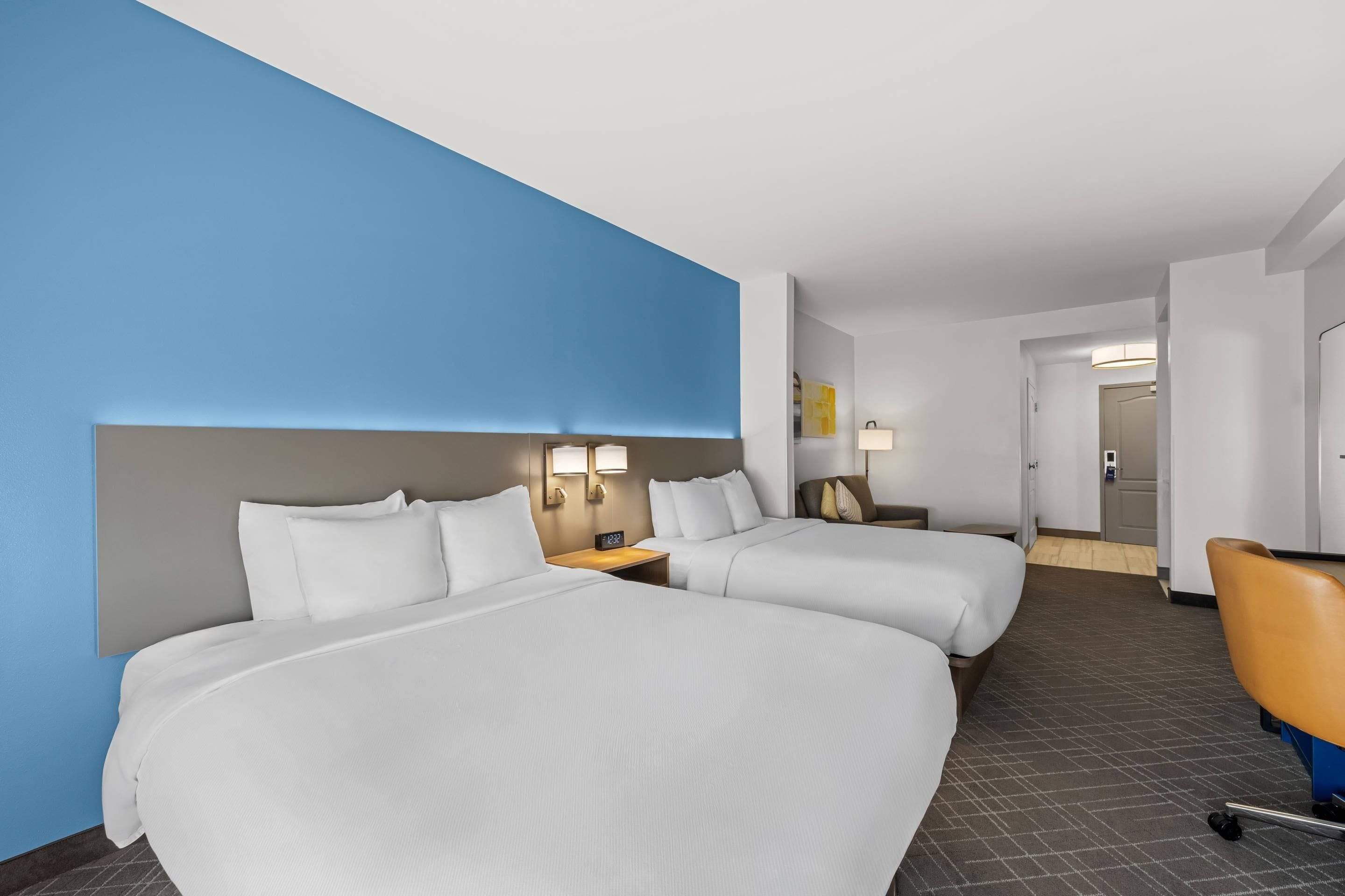 Habitació d'hotel amb dos llits, una escriptori, una cadira i un bany visible per una porta oberta.