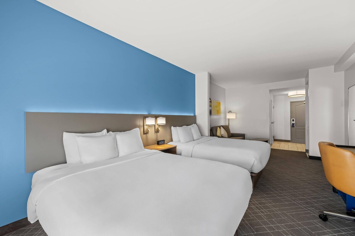 Een hotelkamer met twee bedden, een bureau, een stoel en een badkamer die door een open deur zichtbaar is.