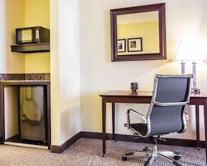 A hotel room with a desk, office chair, microwave, refrigerator, and a mirror with framed pictures.