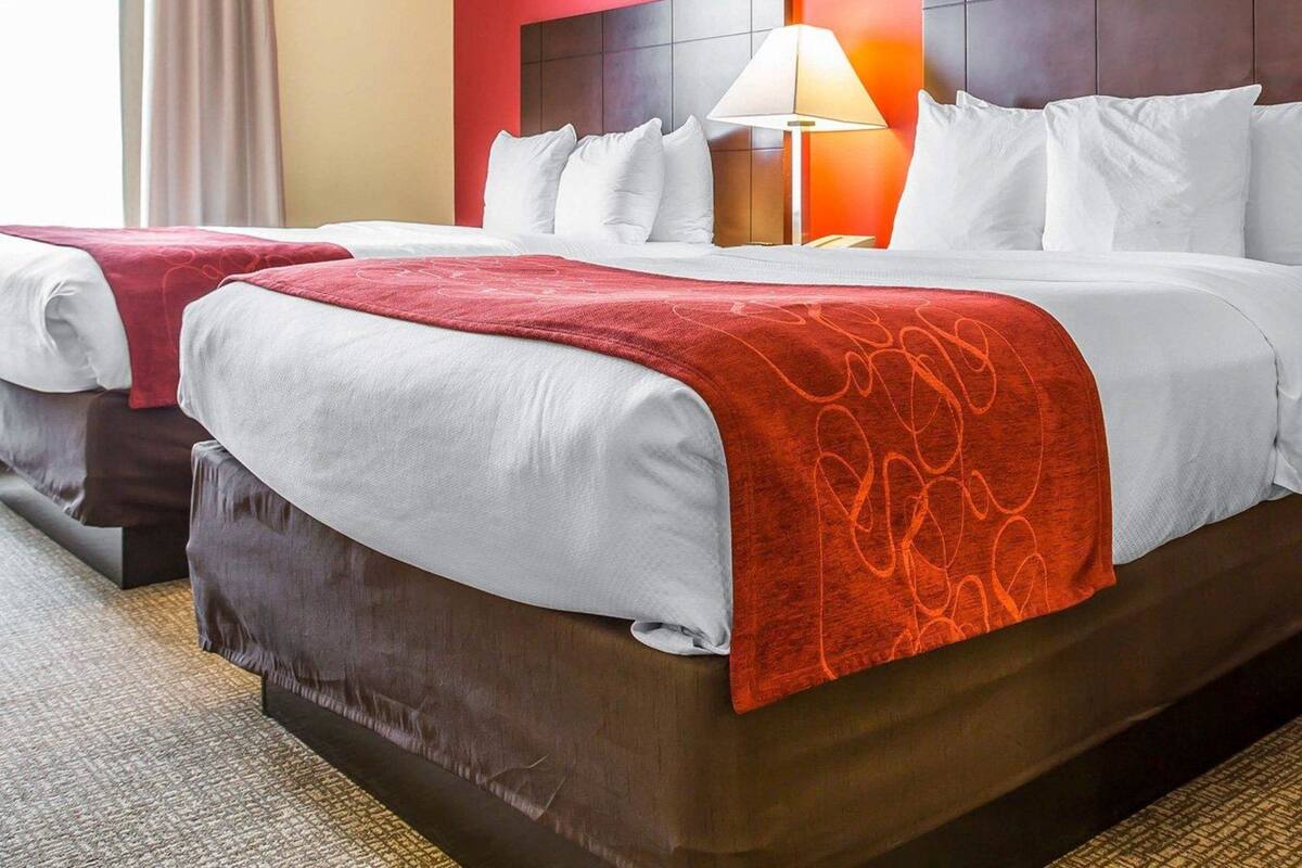 Une chambre d’hôtel avec deux lits, un mur d’accent rouge, une table de chevet avec une lampe et une vue sur l’extérieur.