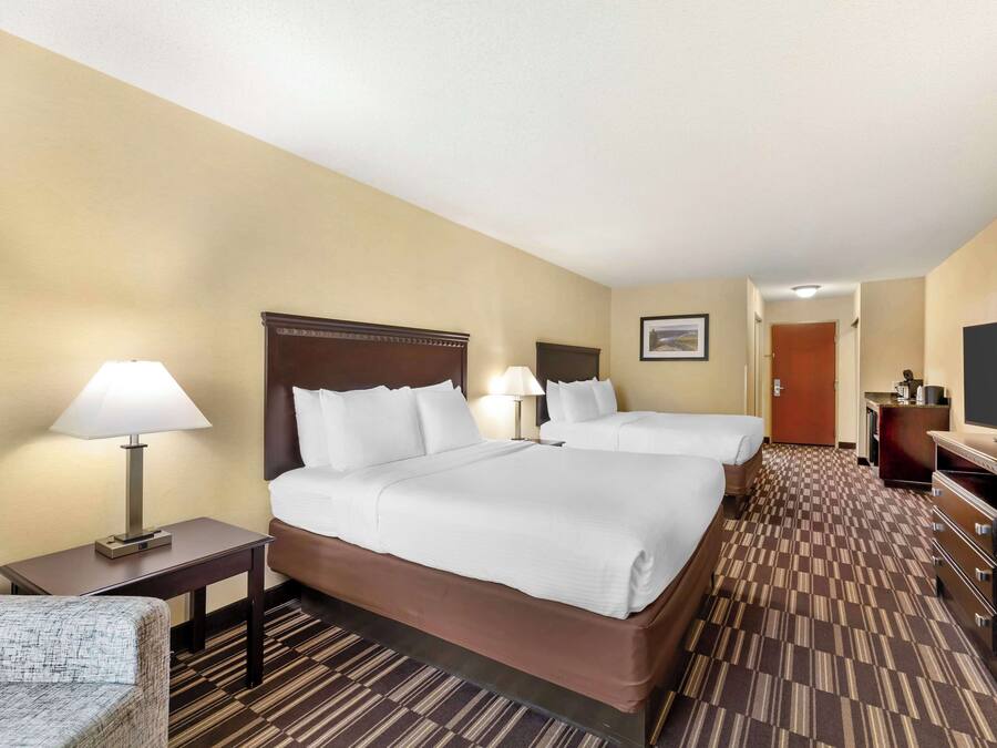 A hotel room with two beds, a desk with a lamp, a TV, and a dresser.