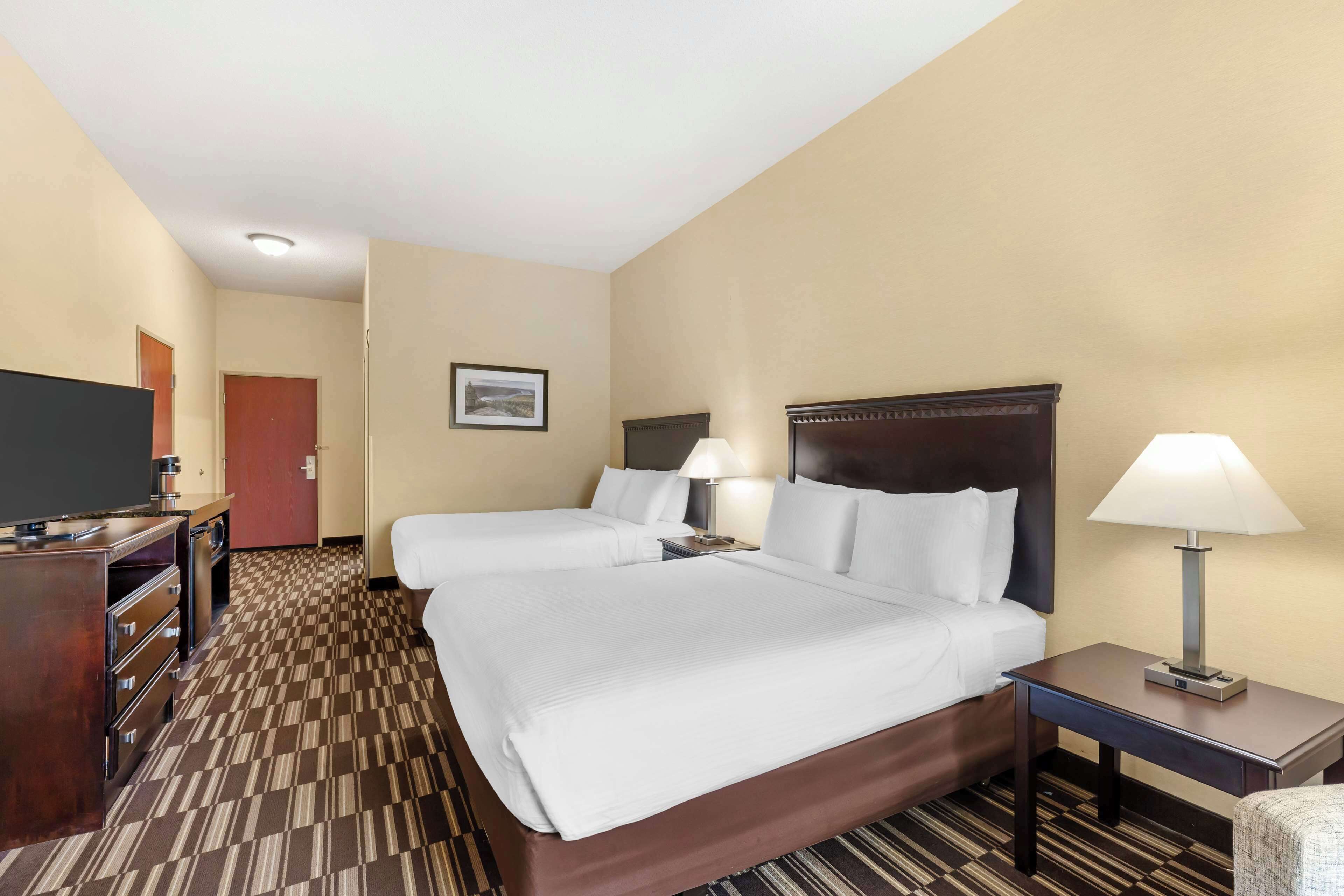 A hotel room with two beds, a desk, a television, and a lamp.