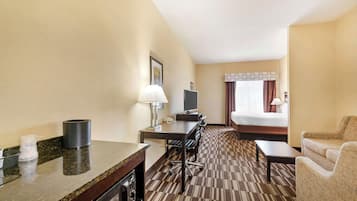 A hotel room with a bed, a desk with a computer, a chair, a coffee maker, and a TV.