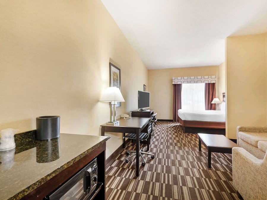 A hotel room with a bed, a desk with a computer, a chair, a coffee maker, and a TV.