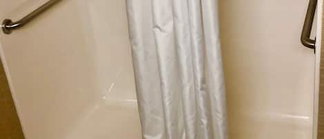 A shower area with a grab bar on the left and a shower curtain.