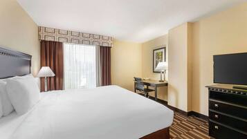 A hotel room with a large bed, a desk, a chair, a television, and a dresser.