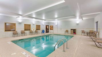 Une grande piscine intérieure à l’eau claire, entourée de chaises longues et de tables.