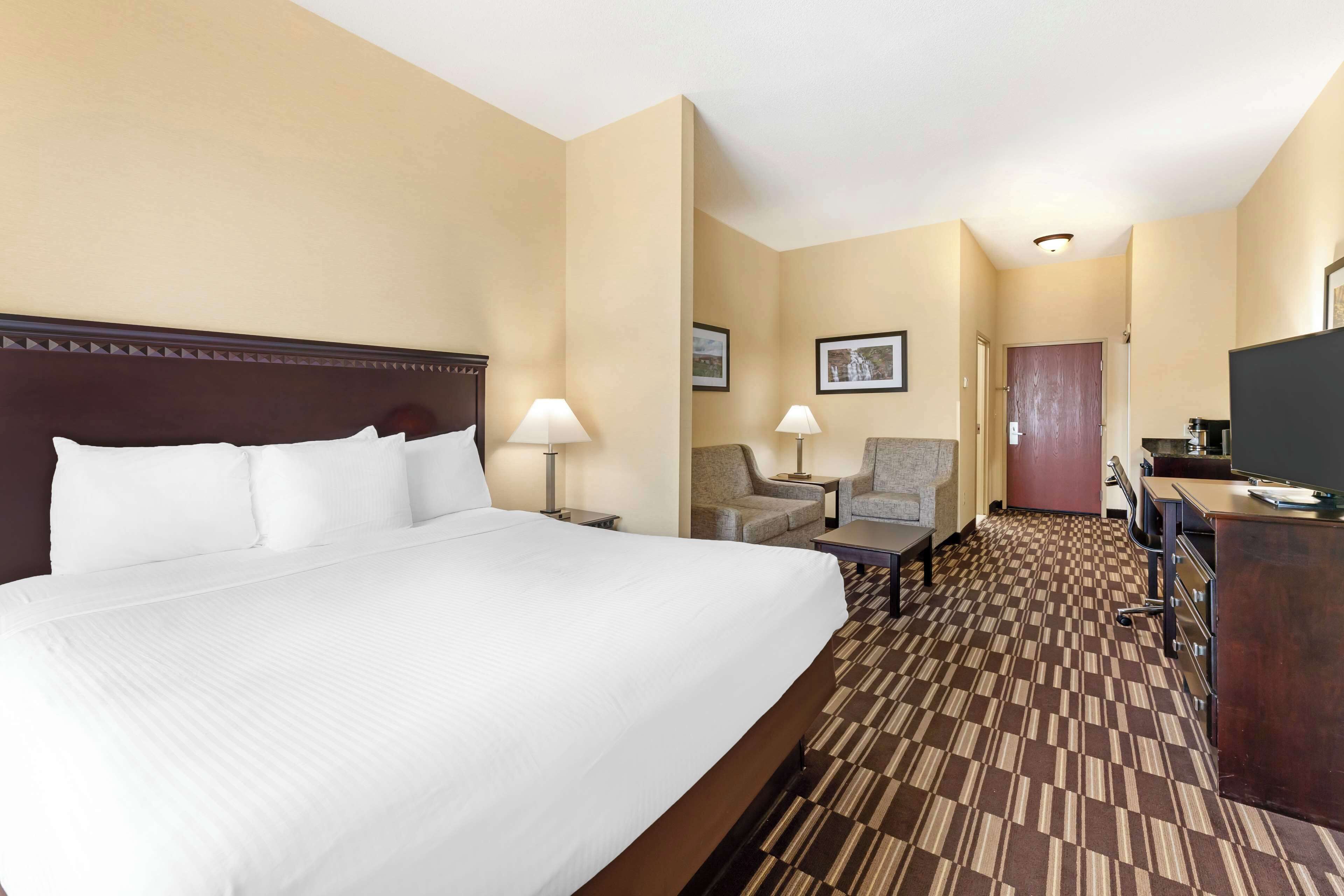Une chambre d’hôtel avec un grand lit, deux fauteuils, un bureau et un téléviseur.