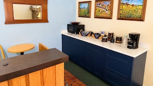 A compact kitchen with a marble countertop, wooden cabinets, a dining table, and a mirror.