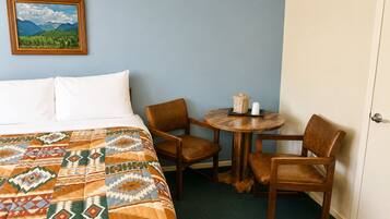 A hotel room with a bed, two chairs, a small table with a teapot, and a framed picture on the wall.