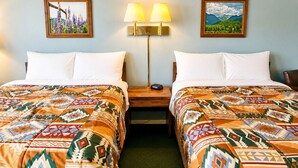 A hotel room with two beds, each with patterned bedding, a nightstand with a lamp, and two framed pictures on the walls.