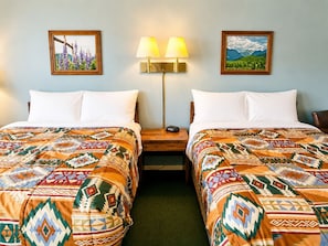 A hotel room with two beds, each with patterned bedding, a nightstand with a lamp, and two framed pictures on the walls. - Branding Iron Motel (Chama)