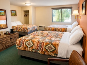 A hotel room with two beds, a dresser, a mirror, a window with a view, and a lamp. - Branding Iron Motel (Chama)