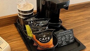 A coffee maker, a tray with coffee pods, a cup, and a coffee maker instruction manual on a wooden table.