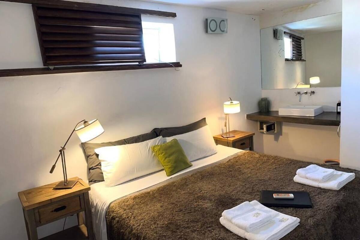 Hotellihuone, jossa on sänky, yöpöydällä olevat lamput, yöpöytä, peili, pesuallas ja pyyhkeet.