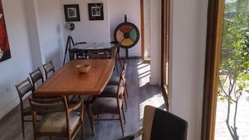 Zona pranzo con tavolo e sedie in legno, ventilatore a soffitto e finestra vista verde.