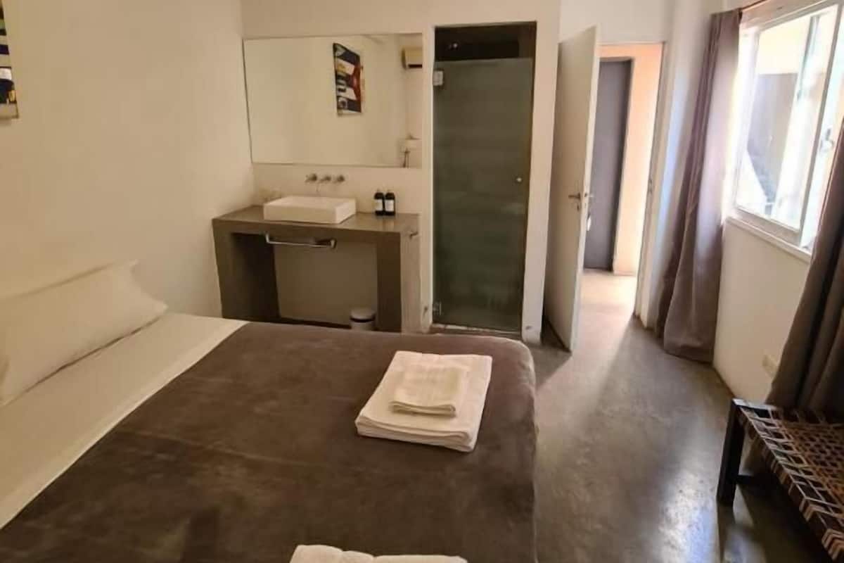 Hotellihuone, jossa on sänky, työpöytä, peili, kylpyhuone ja ikkuna.