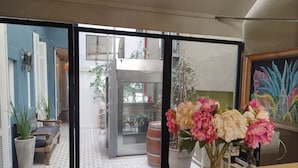 A room with a view through a glass partition to an outdoor area with a door, potted plants, and a tiled floor. - Hotel Costa Rica (Buenos Aires)