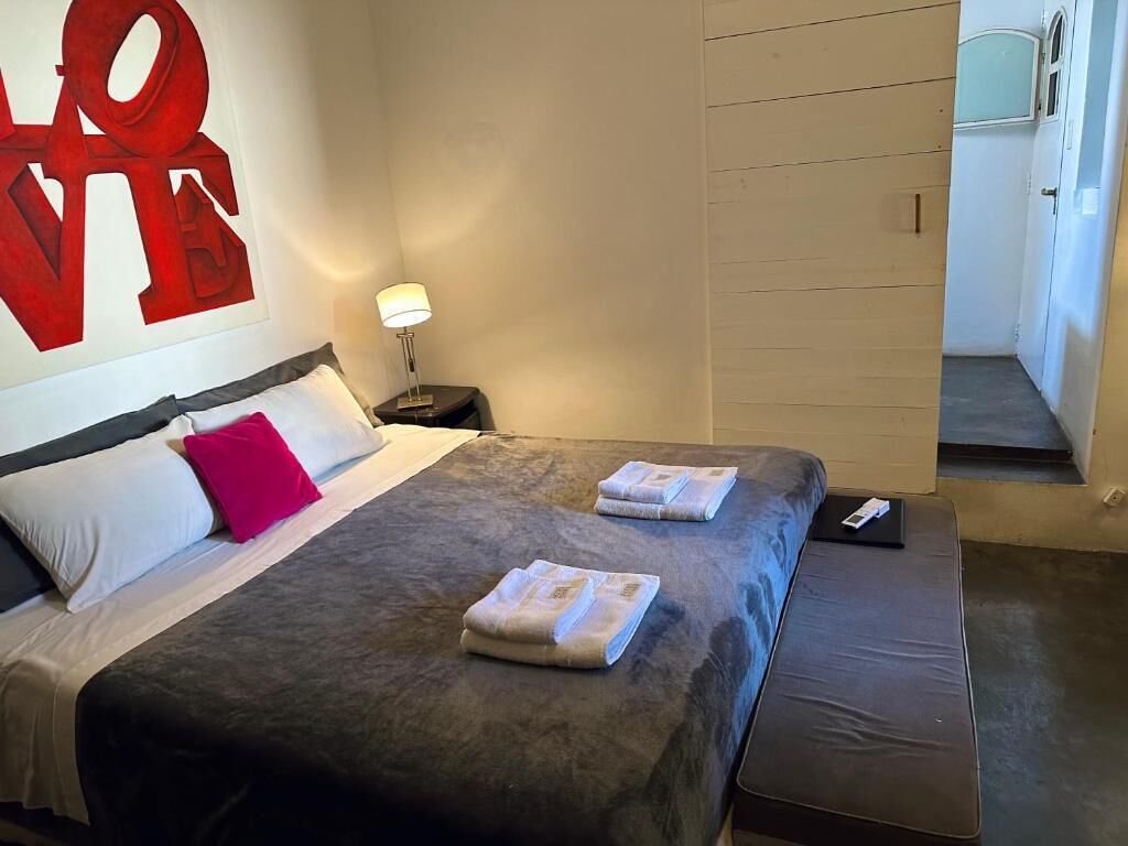 A hotel room with a large bed, a nightstand, a lamp, and a view of the hallway.