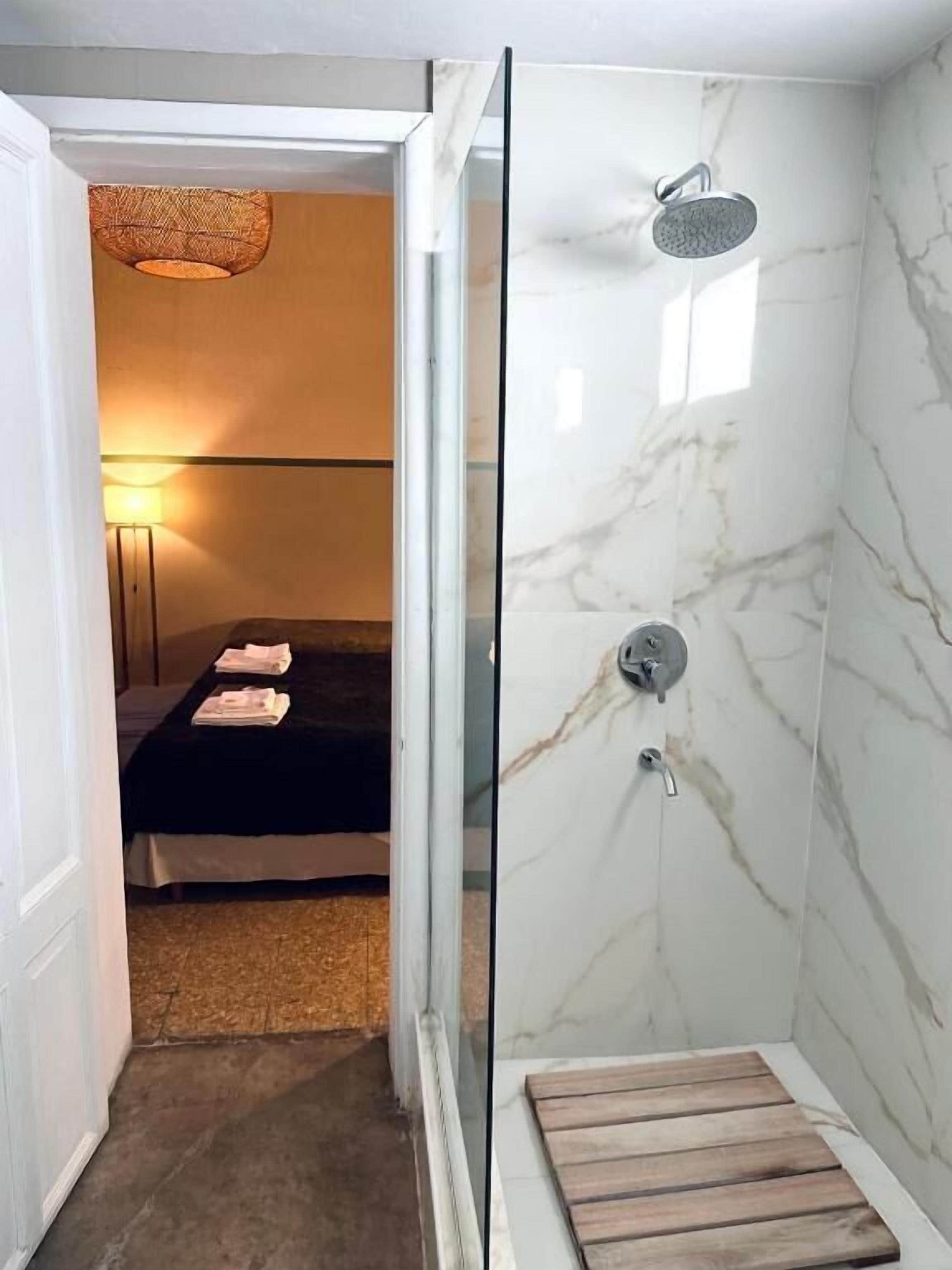 Een kamer met een bed, een houten bankje, een douche met glazen deur en een lamp.