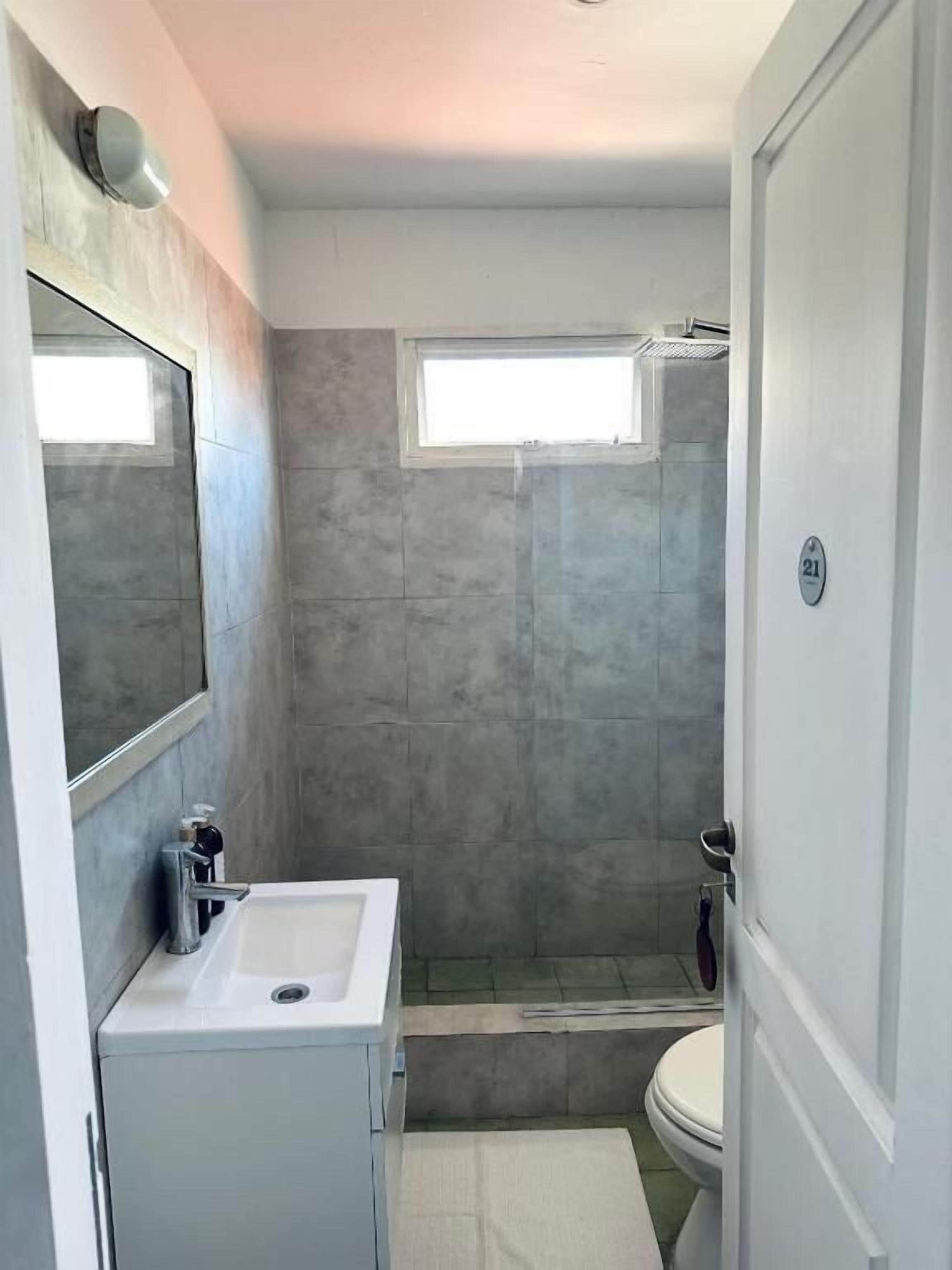 A compact bathroom with a white sink, a mirror, a shower, and a toilet.