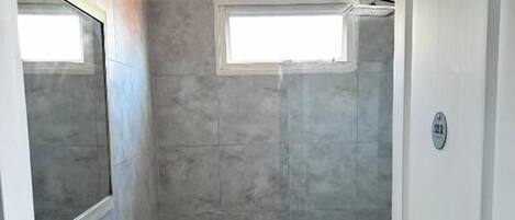 A compact bathroom with a white sink, a mirror, a shower, and a toilet.