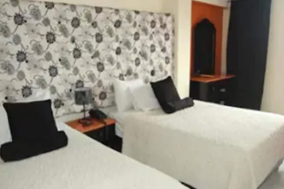A hotel room with two beds, a nightstand, a lamp, and a mirror.