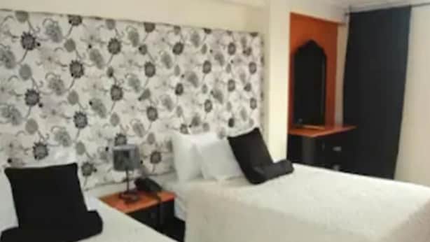 Una habitación de hotel con dos camas, una mesita de noche, una lámpara y un espejo.