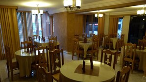 Un comedor con varias mesas redondas y sillas de madera, con candelabros y ventanas amplias con cortinas.