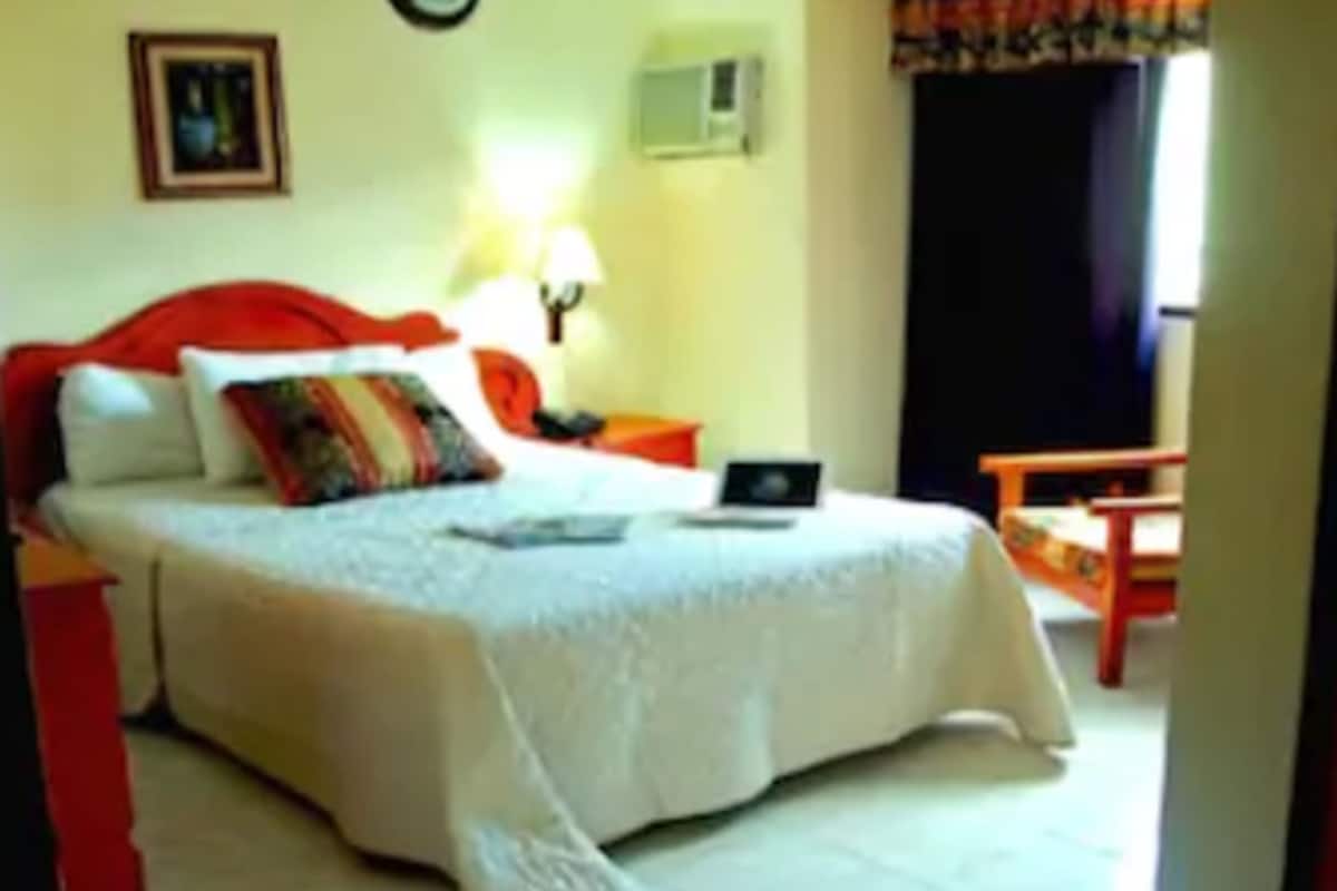 A hotel room with a bed, a laptop, a chair, a lamp, and a window with curtains.