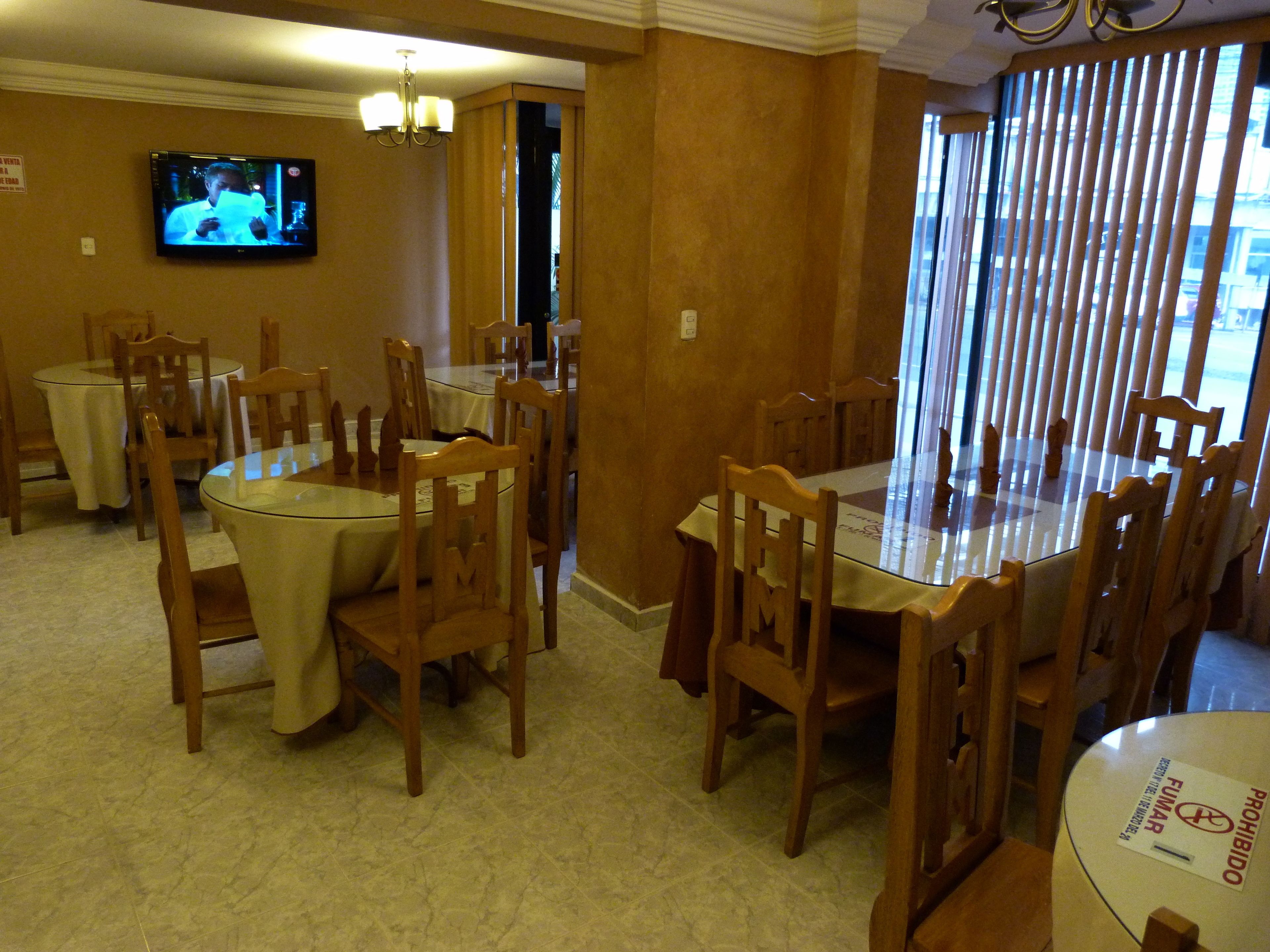 Un espace repas avec des tables rondes et des chaises en bois, un téléviseur fixé au mur et un lustre.