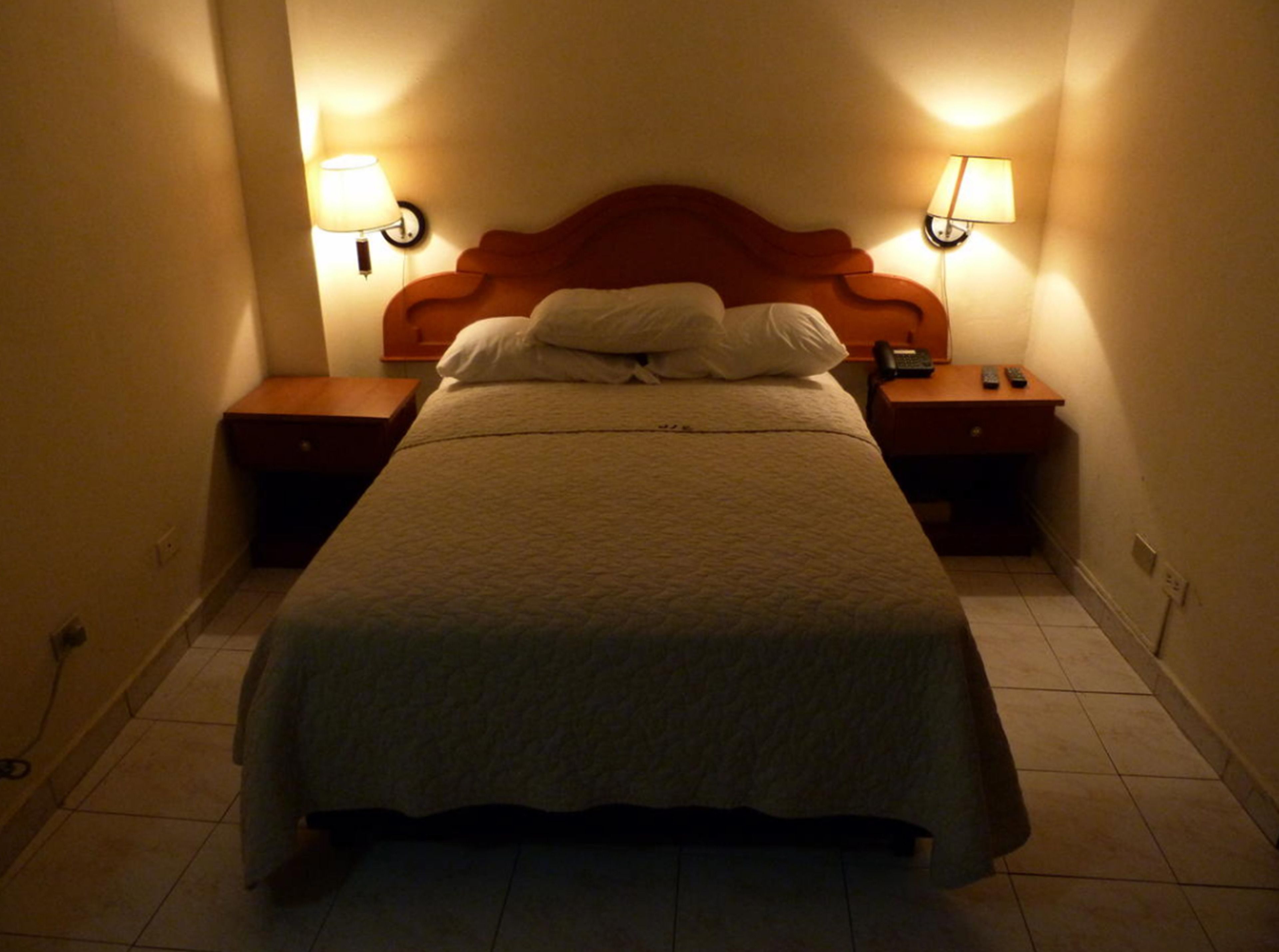 A standard hotel room with a single bed, two bedside tables, a nightstand, and two wall-mounted lamps.