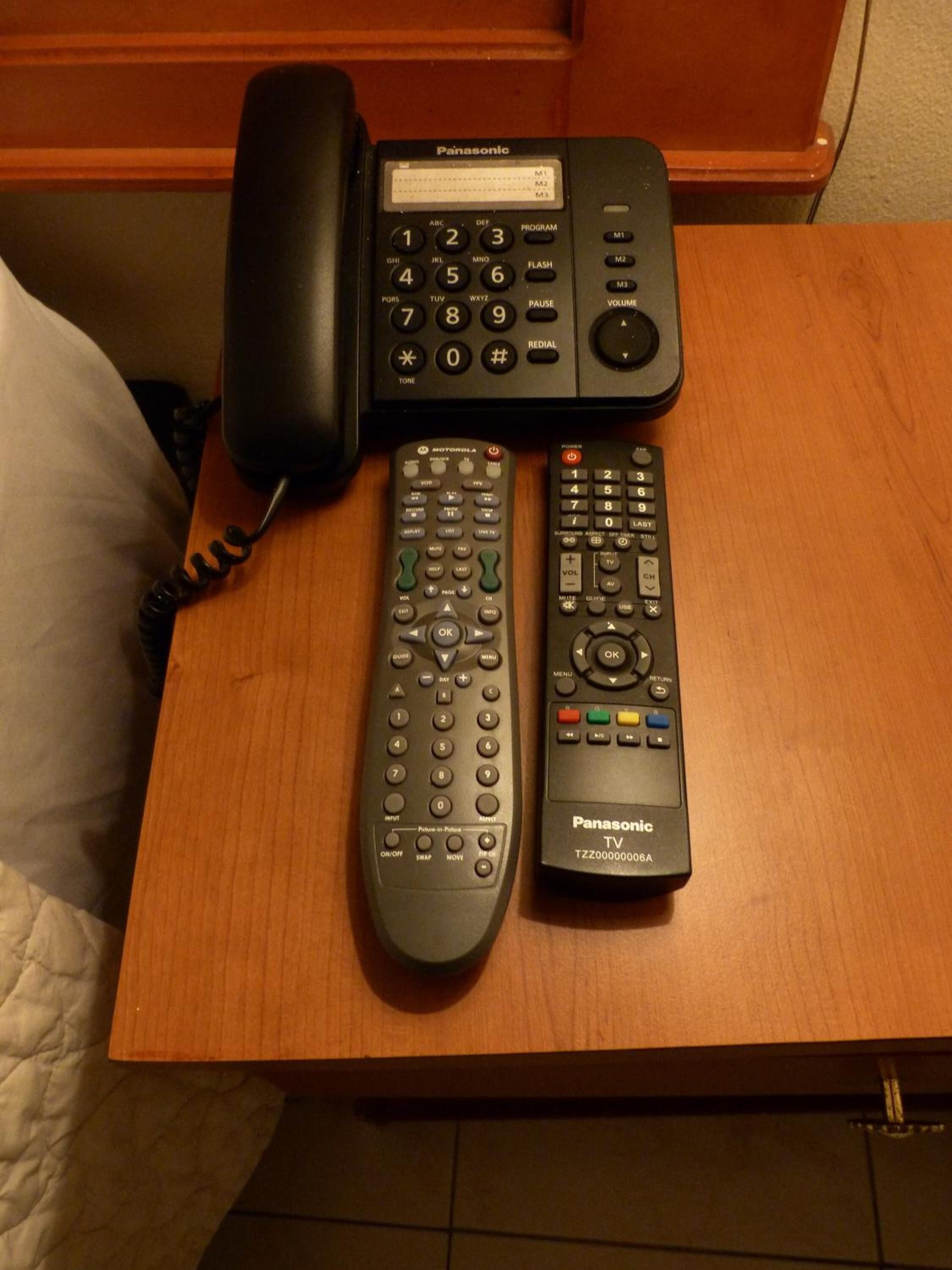A wooden nightstand with a Panasonic TV remote and a Panasonic phone on it.