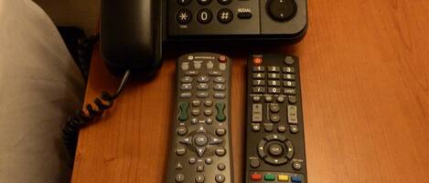 A wooden nightstand with a Panasonic TV remote and a Panasonic phone on it.