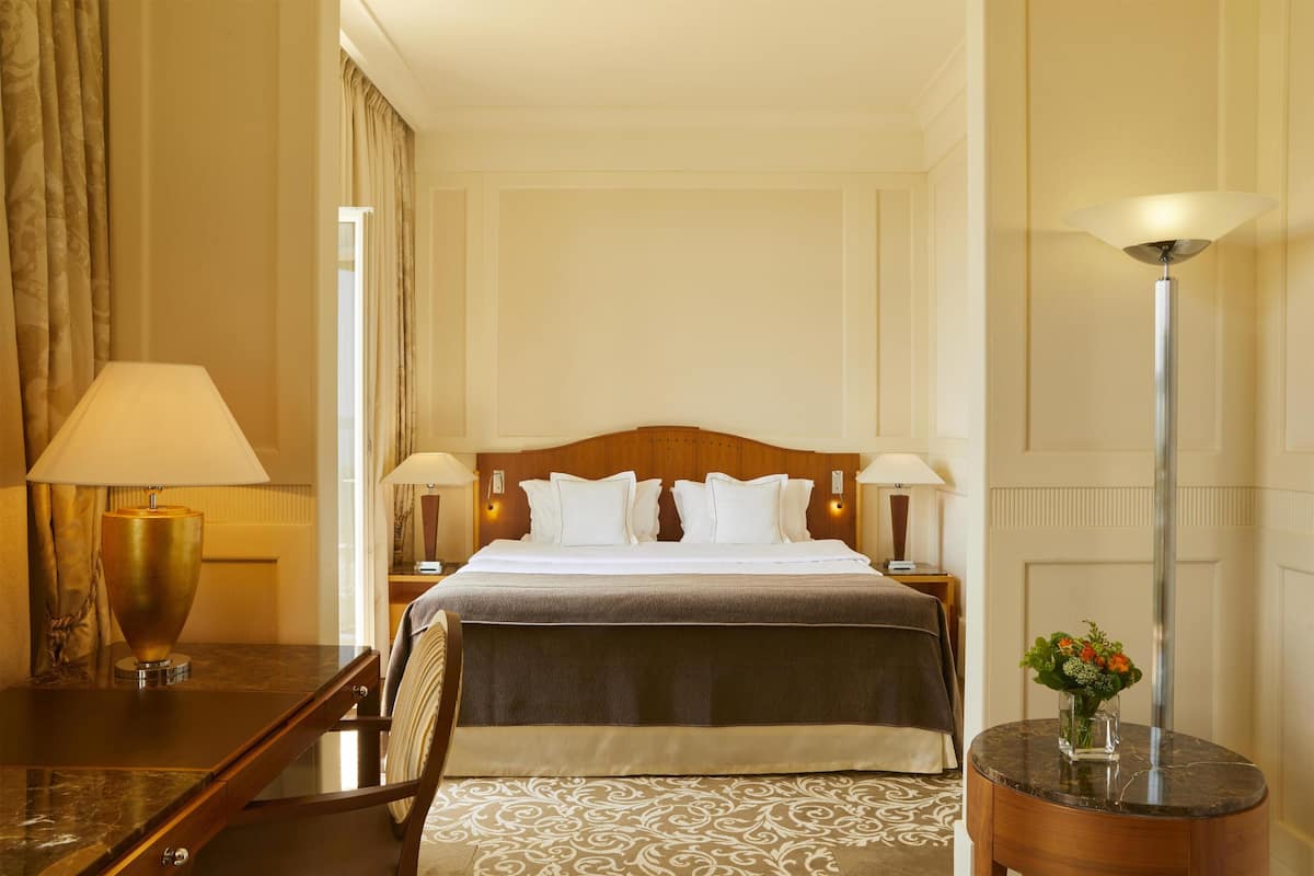 Ein Hotelzimmer mit Bett, Schreibtisch, Stuhl, Lampe und einer Blumenvase.
