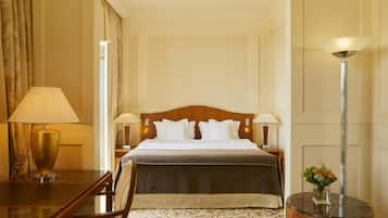 A hotel room with a bed, a desk, a chair, a lamp, and a vase with flowers.