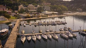 A marina with boats docked, a hotel named 'Palace Hotel' in the background, and a hillside with buildings. - Hotel Palace Portoroz Operated by Minor Hotels (Piran)