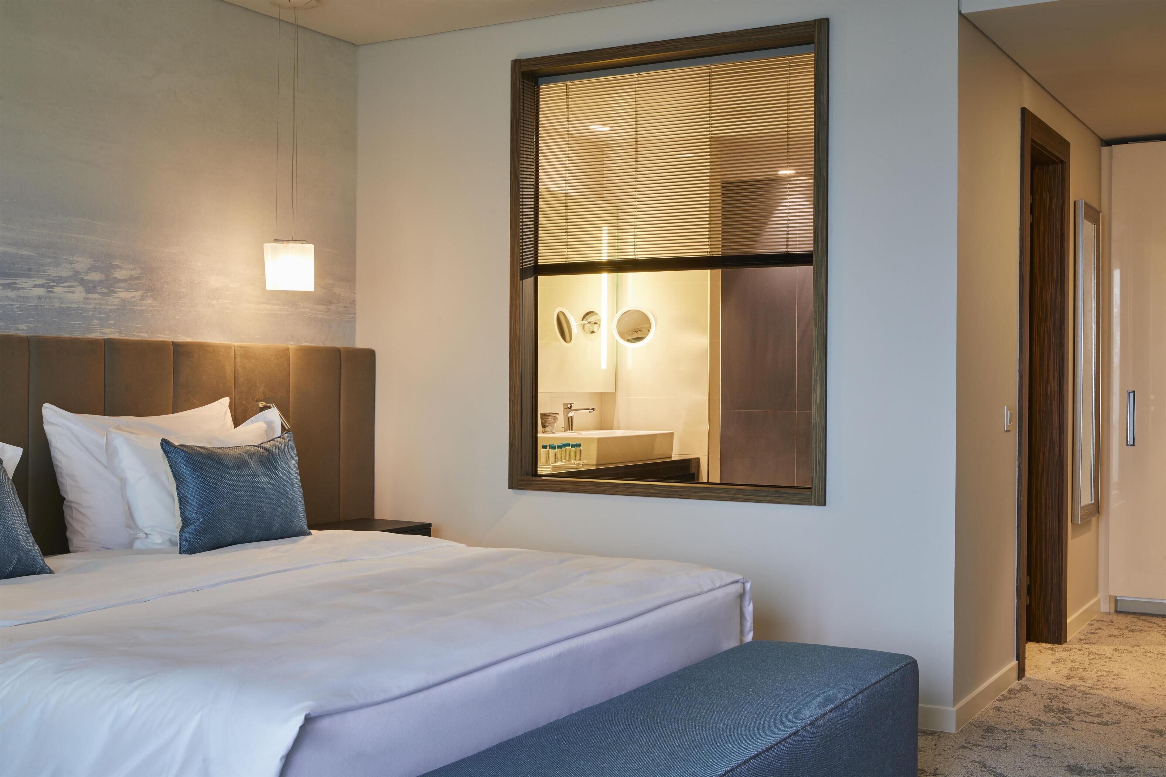 A hotel room with a large bed, a bedside table, a mirror, and a view of a bathroom.