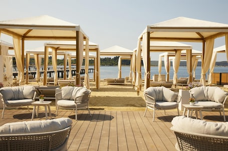 A beachside lounge with wooden pergolas, wicker furniture, and a view of the water.