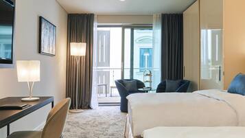 Habitación de hotel con cama, escritorio, silla, lámpara y vistas al exterior.
