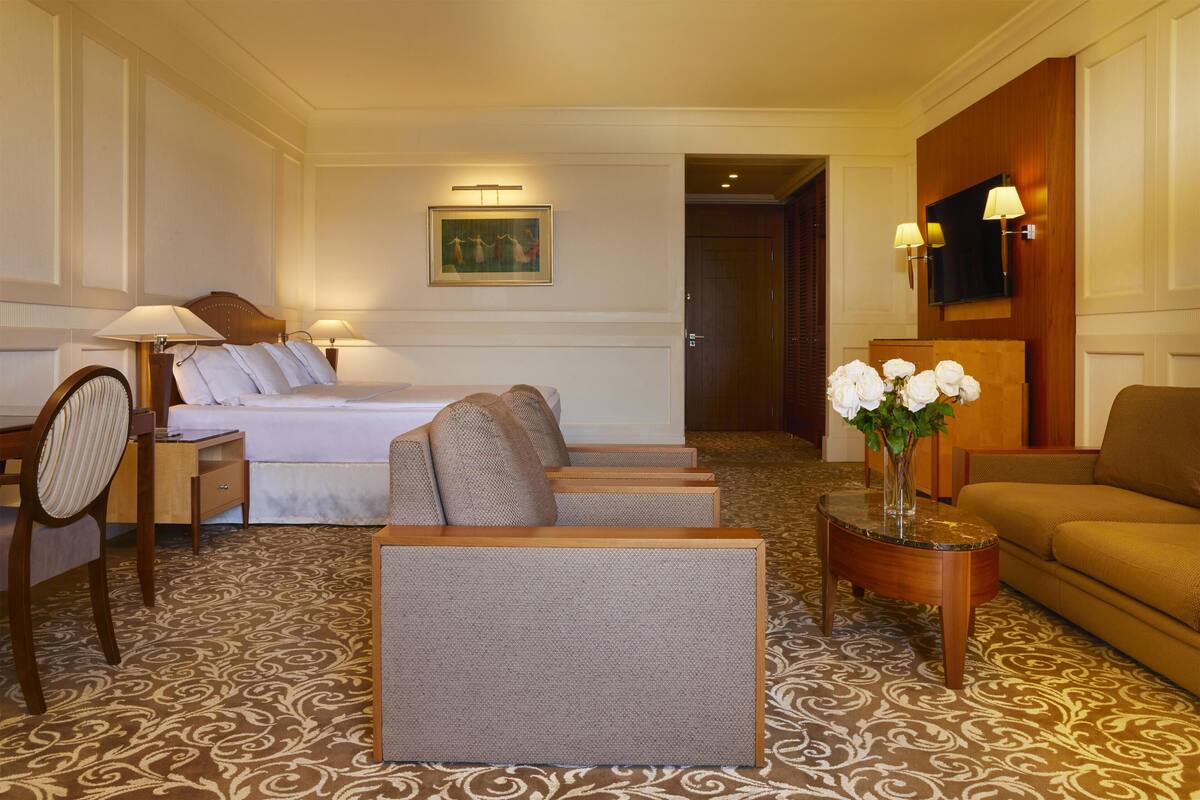 Ein Hotelzimmer mit einem Bett, zwei Sesseln, einem Sofa, einem kleinen Tisch mit einer Vase und einem Fernseher.