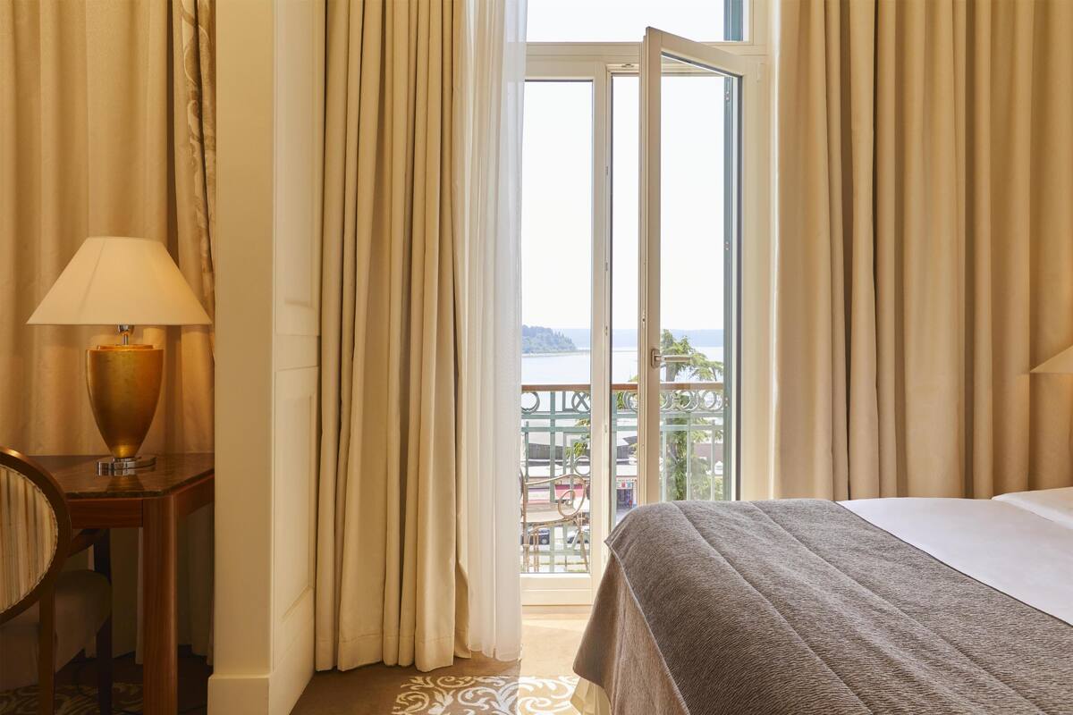 Ein Hotelzimmer mit Bett, Lampe, Blick ins Freie und Vorhängen.