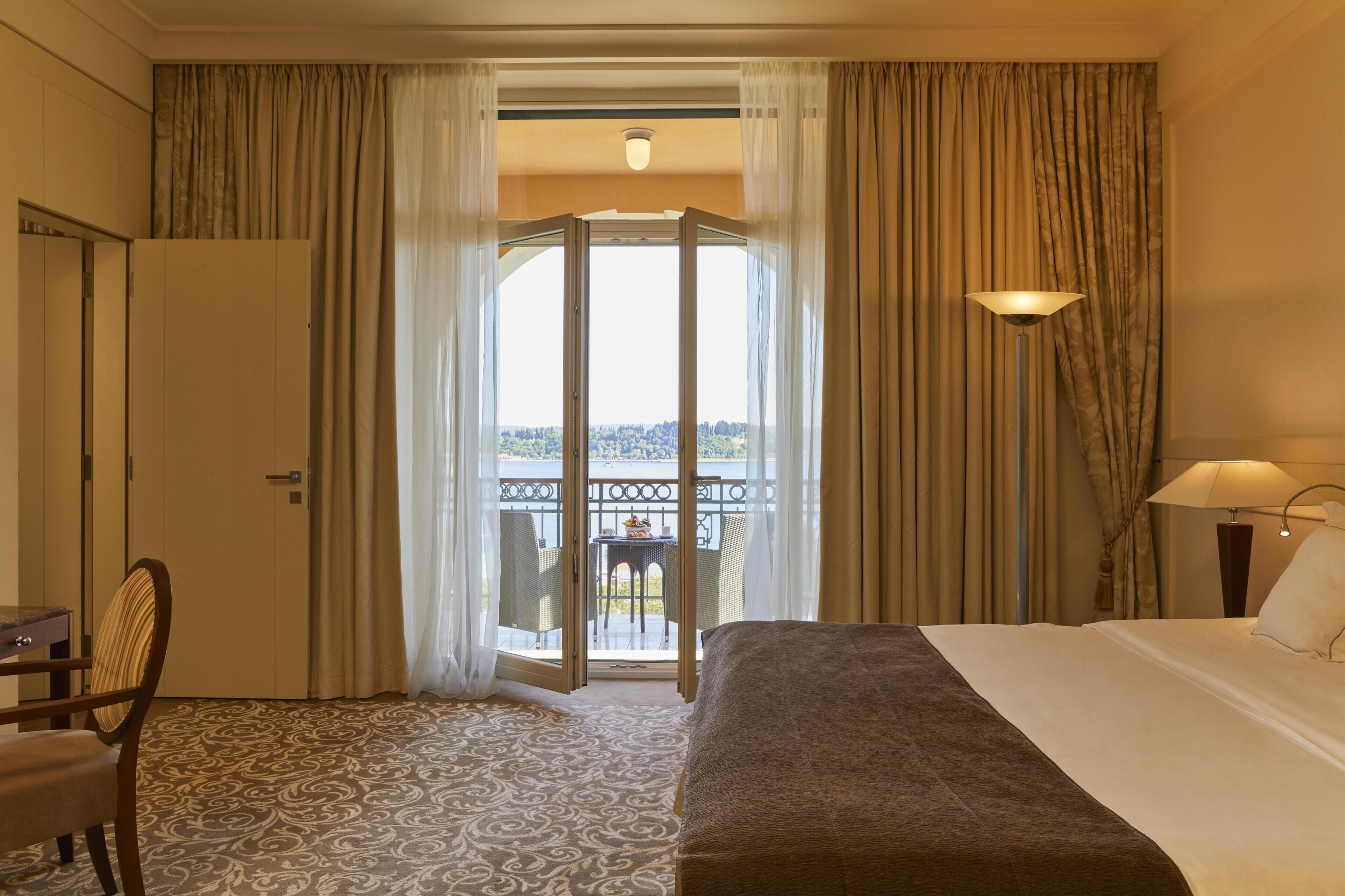 Habitación de hotel con cama, escritorio, silla, balcón con mesa y sillas, y cortinas.