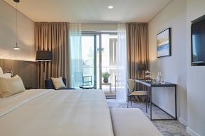 Habitación de hotel con una cama grande, un escritorio, una silla, una mesita, una lámpara, una planta en maceta y vistas al exterior.
